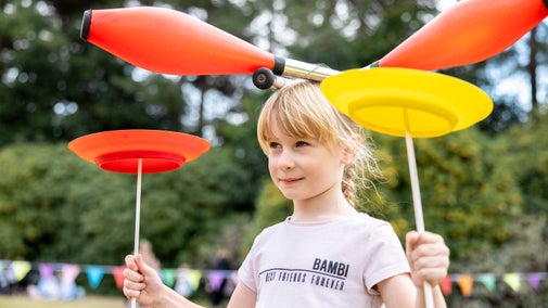 A young girl practising plate spinning while also balancing juggling clubs on her head